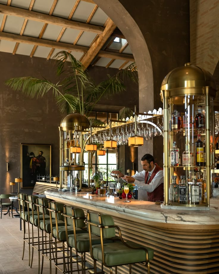 a man is behind the bar at a restaurant with green chairs and gold fixtures on it