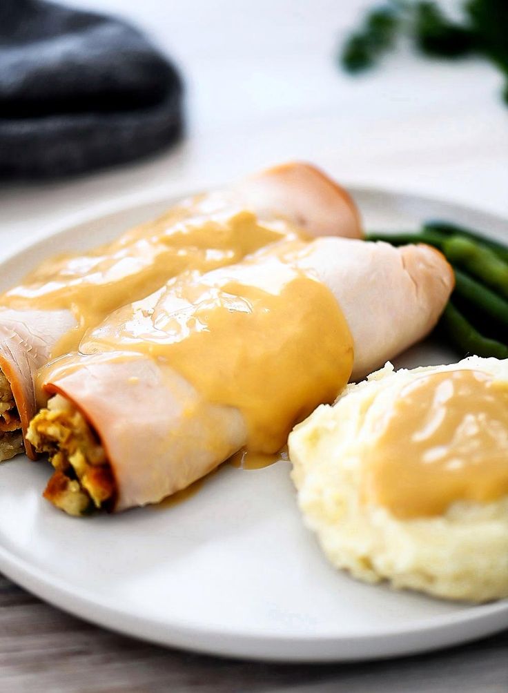 a plate with mashed potatoes, asparagus and ham wrapped in cheese sauce