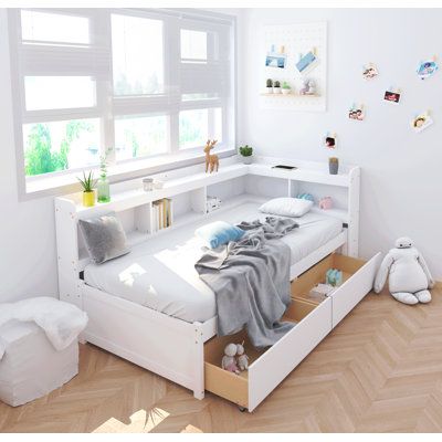 a white bed with drawers underneath it and stuffed animals on the floor next to it