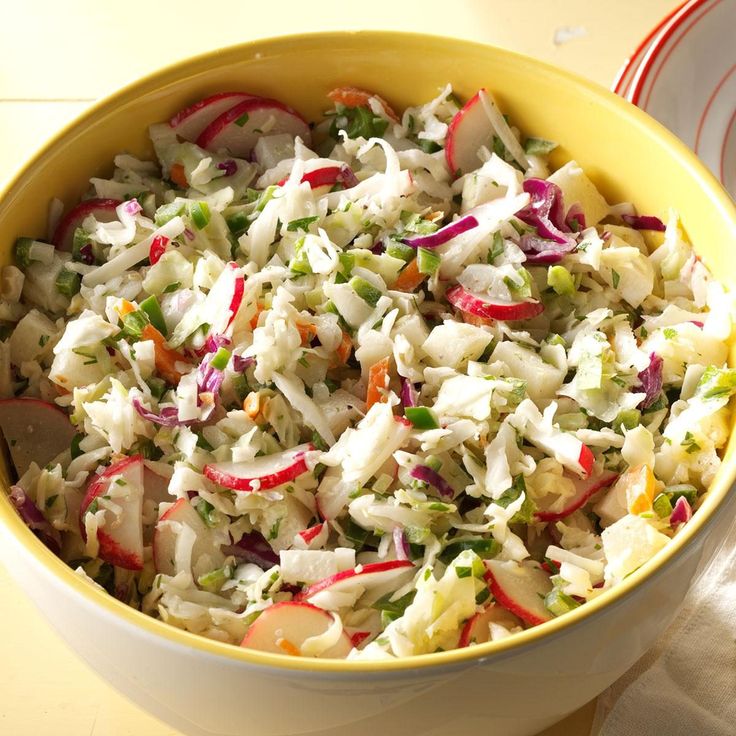 a bowl filled with coleslaw next to a white plate and napkin on a table