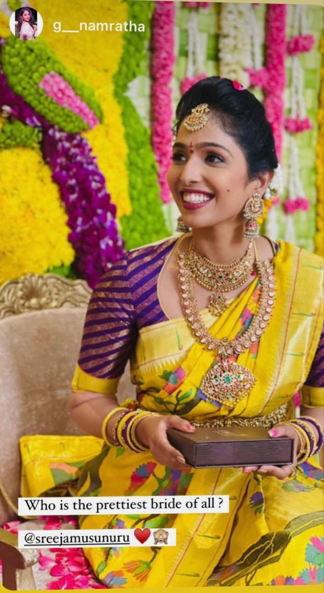 a woman in yellow sari sitting on a couch holding a box with flowers behind her