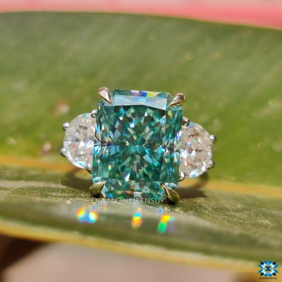 an emerald and diamond ring sitting on top of a leaf