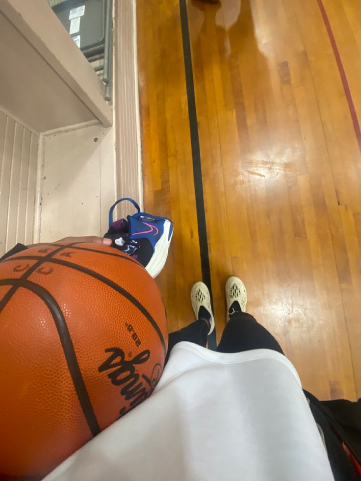 an orange basketball sitting on top of a wooden floor next to a person's feet