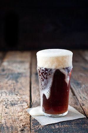 a tall glass filled with liquid sitting on top of a wooden table next to a napkin