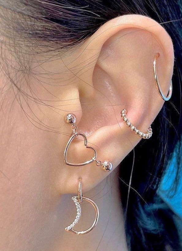 a close up of a person wearing ear piercings with an open heart and moon design