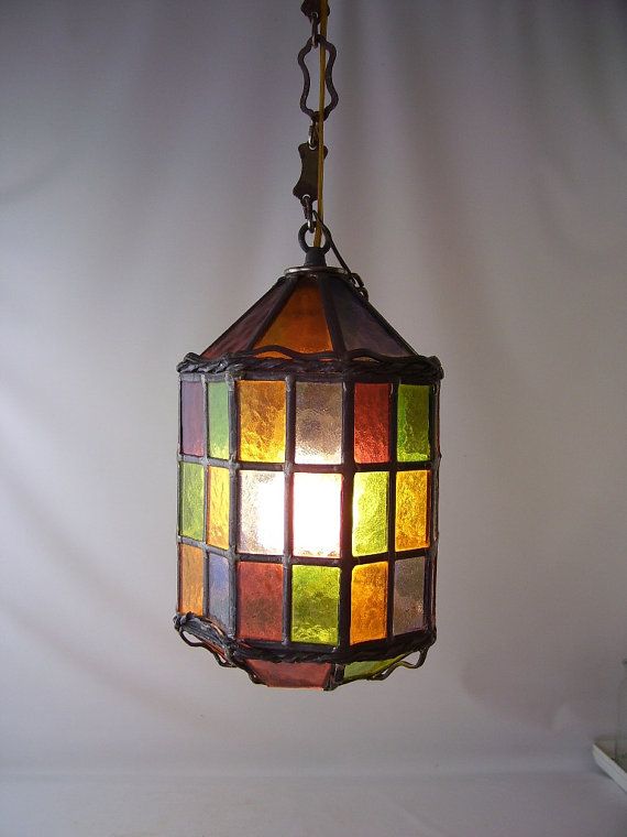 a multicolored stained glass light hanging from a metal chain on a white wall