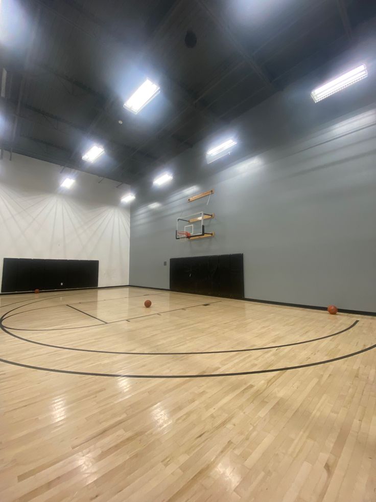 an indoor basketball court with hard wood flooring and lights on the ceiling, surrounded by white walls