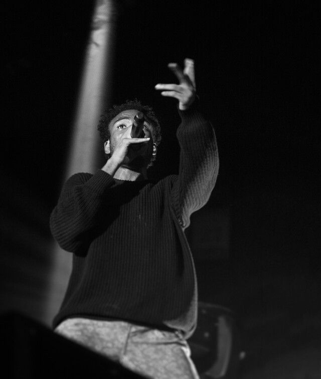 a man standing on top of a stage holding his hand up in the air while talking on a cell phone