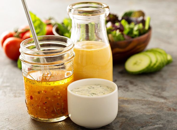 there are many different types of dressings in jars on the table with cucumbers, tomatoes and lettuce