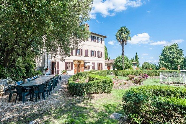 an outdoor dining table and chairs in front of a large house with trees around it