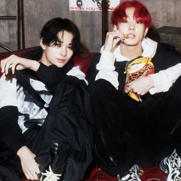 two young men sitting on top of a red couch next to each other, one with bright red hair