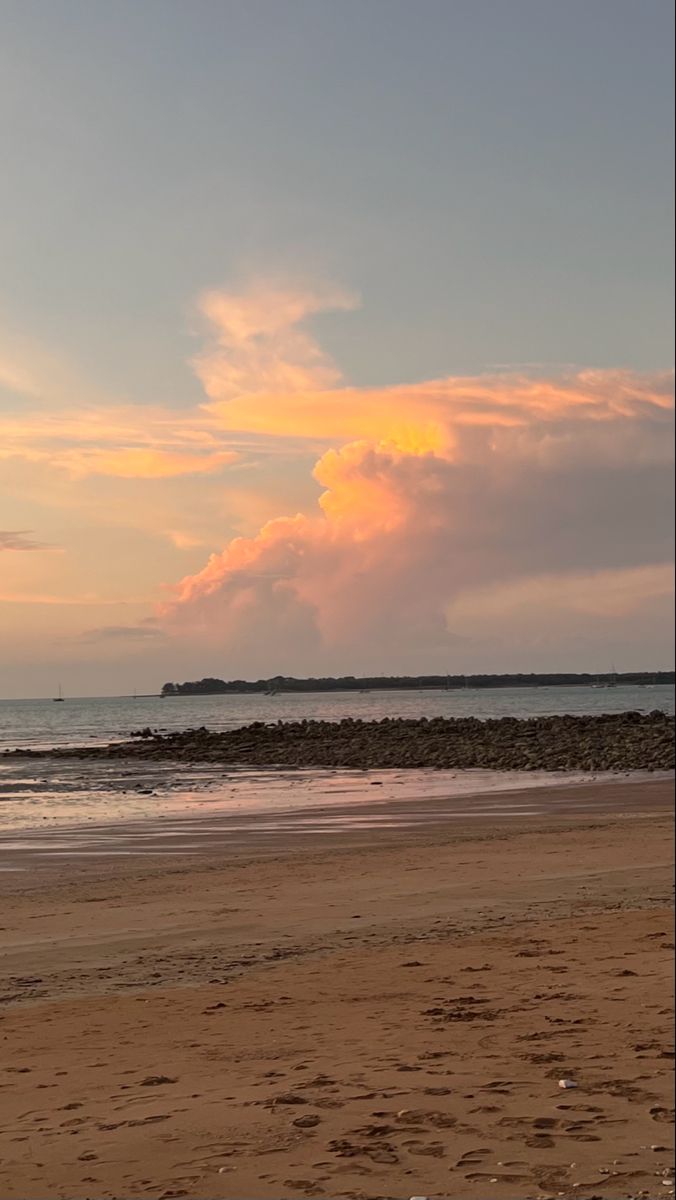 a person walking on the beach with a surfboard under an orange and pink sky