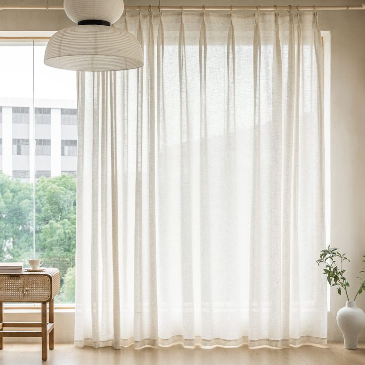 a living room filled with furniture and a large window covered in white drapes next to a wooden table