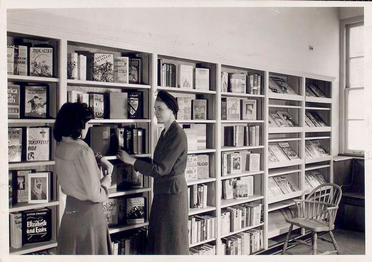 two women standing in front of a book shelf filled with books