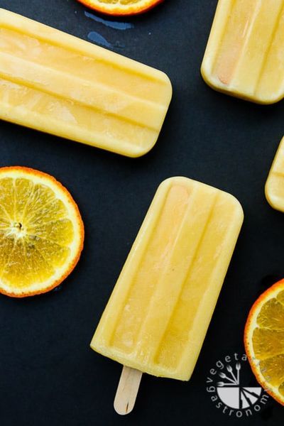 three popsicles with orange slices cut in half on a black surface next to an orange slice