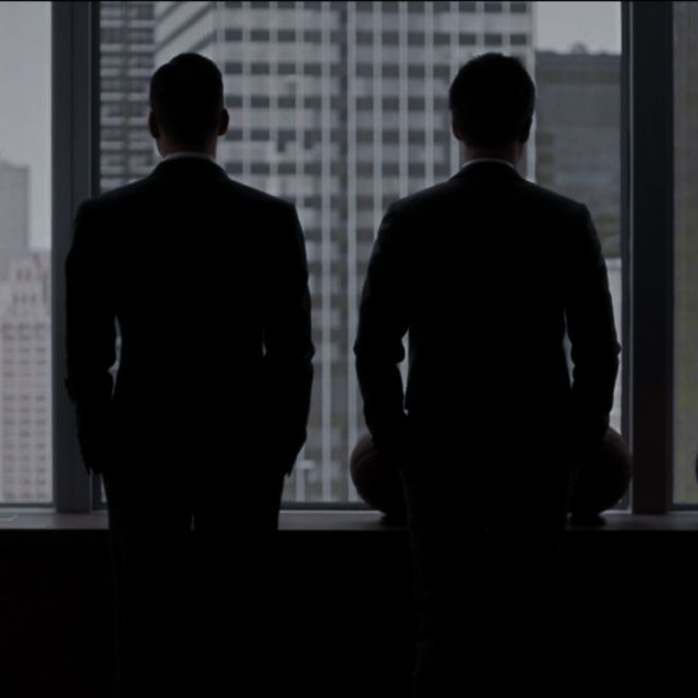 two men standing in front of a large window looking out at the city below them