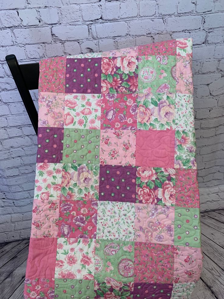 a pink and green patchwork quilt sitting on top of a black chair next to a brick wall