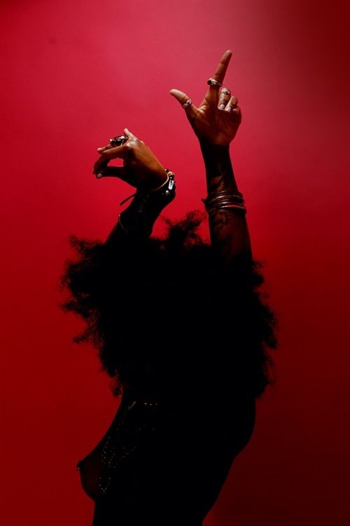 a woman making the peace sign with her fingers on top of her head, against a red background