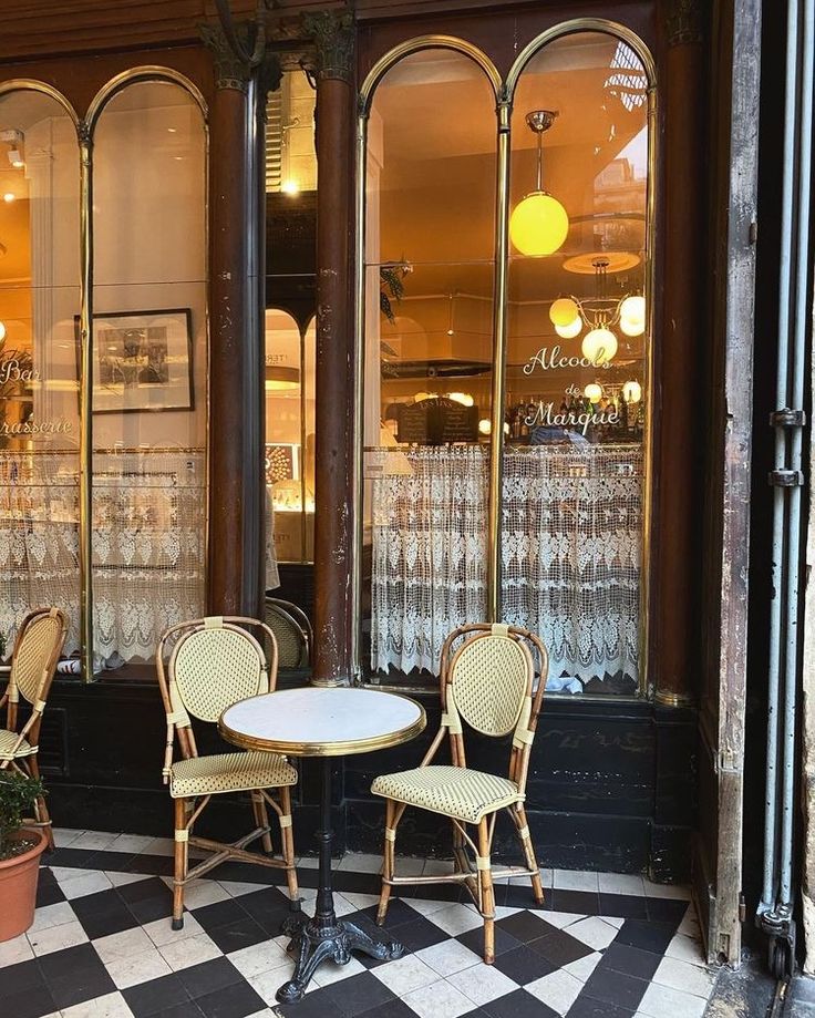 two chairs and a table sitting in front of a store window with wine glasses on it