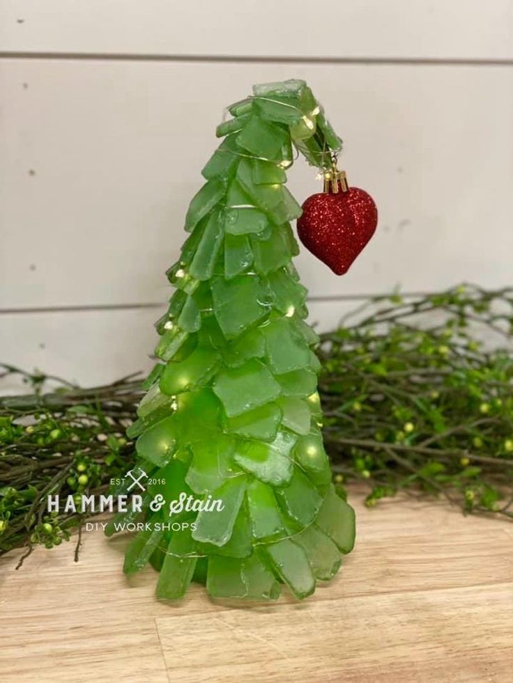 a green christmas tree with a red heart hanging from it's side on a wooden table