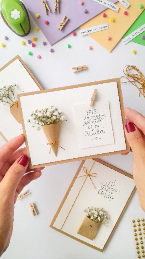 two hands holding cards with flowers in them and some confetti on the table