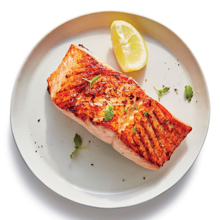 a piece of grilled salmon on a plate with lemon wedges and parsley