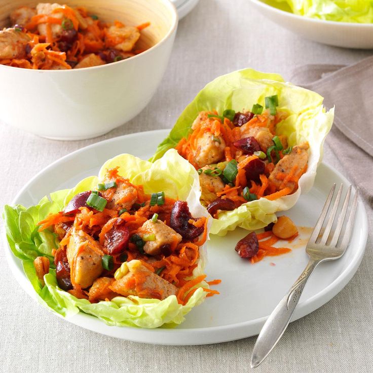 two lettuce cups filled with meat and vegetables next to a bowl of salad