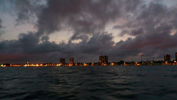 the city lights shine brightly in the distance as dark clouds loom over the water