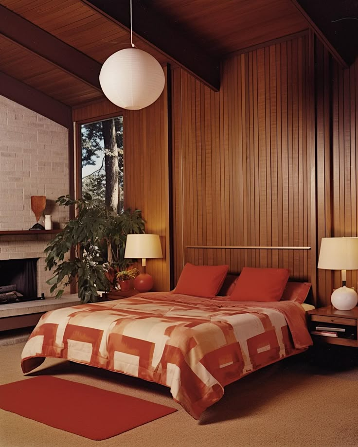 a bedroom with wood paneling and red bedspread in front of a fireplace