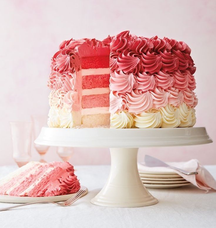 a pink and white cake sitting on top of a plate next to a slice of cake