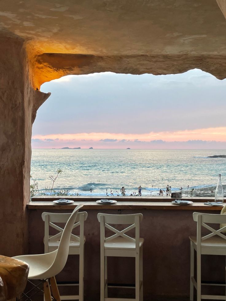 two white chairs sitting next to each other on top of a wooden table near the ocean