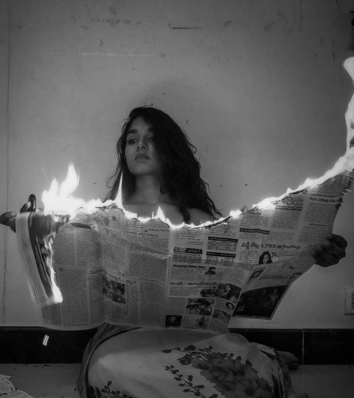 a woman sitting on the floor reading a newspaper with flames coming out of her arms