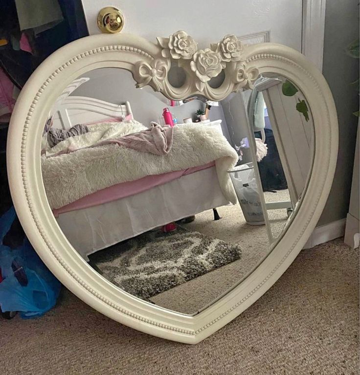 a white heart shaped mirror sitting on top of a carpeted floor next to a bed