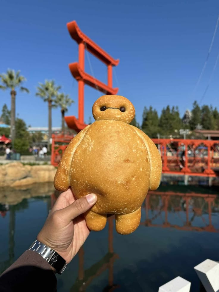 a person holding up a small teddy bear in front of a body of water with an orange structure behind them