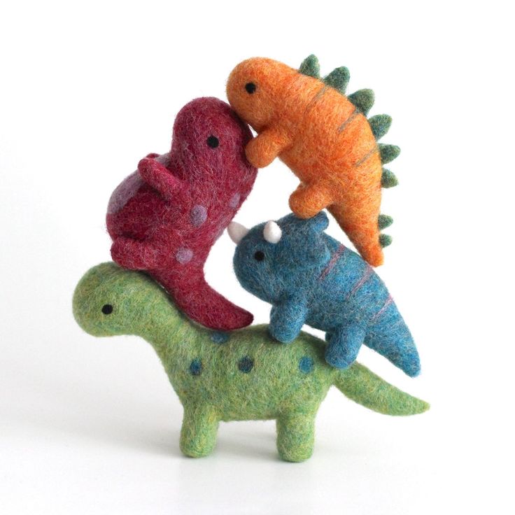 three small stuffed animals sitting on top of each other in the shape of dinosaurs