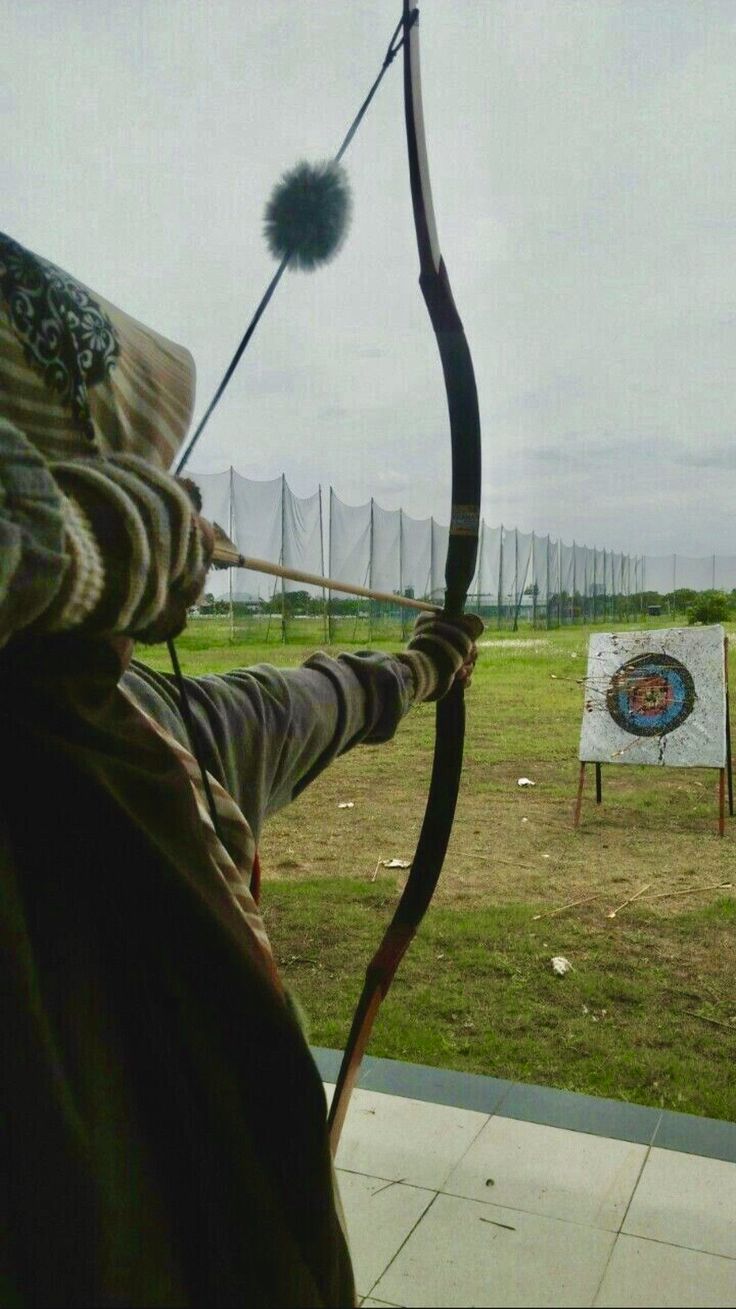 the man is practicing his archery skills in the field by shooting an arrow at target