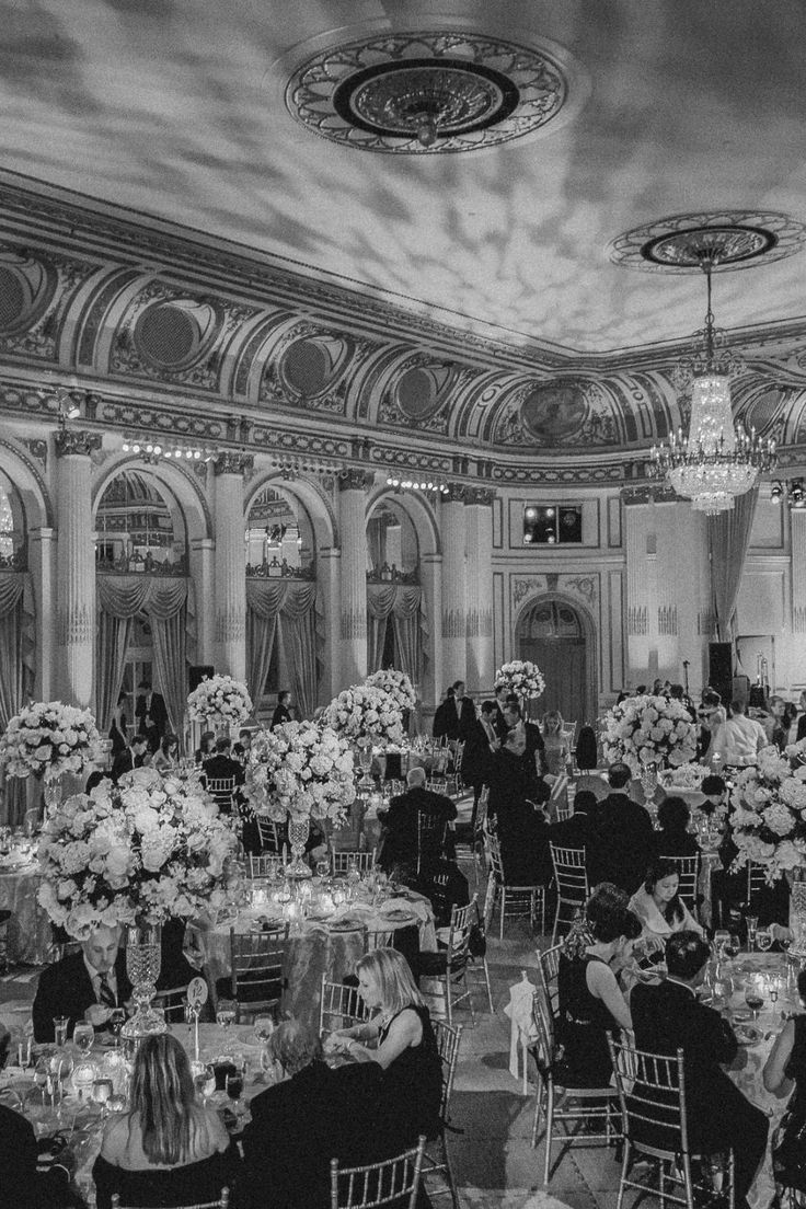 a black and white photo of people sitting at tables in a banquet hall with chandeliers