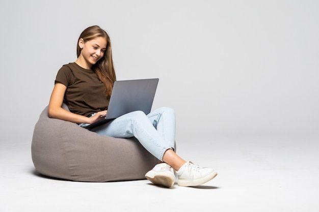 a young woman sitting on a bean bag chair using a laptop computer while looking at the screen