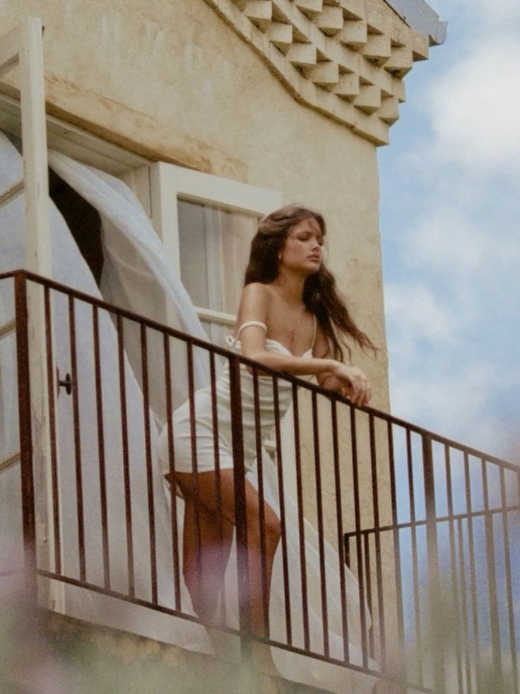 a woman standing on top of a balcony next to a building and looking out the window