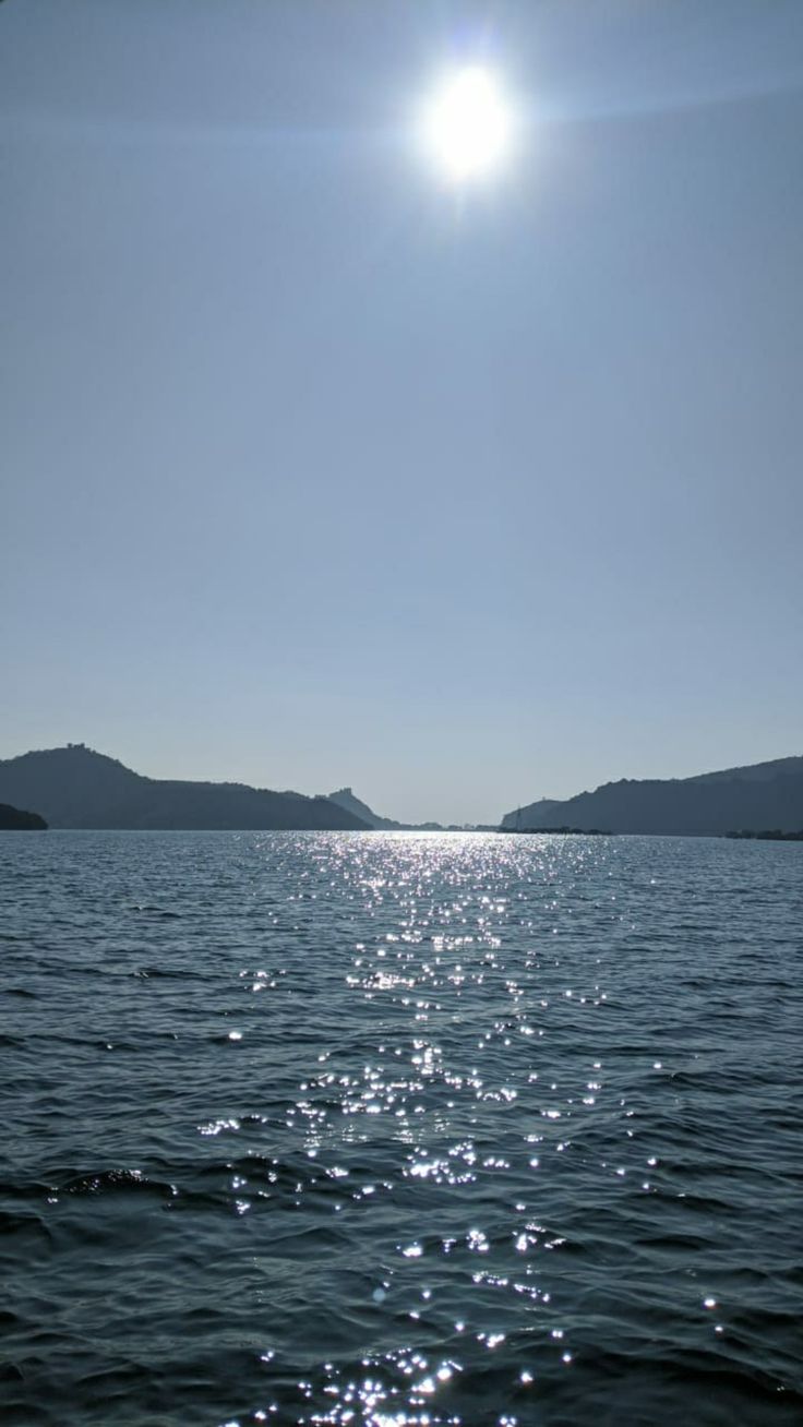 the sun shines brightly over water with mountains in the background