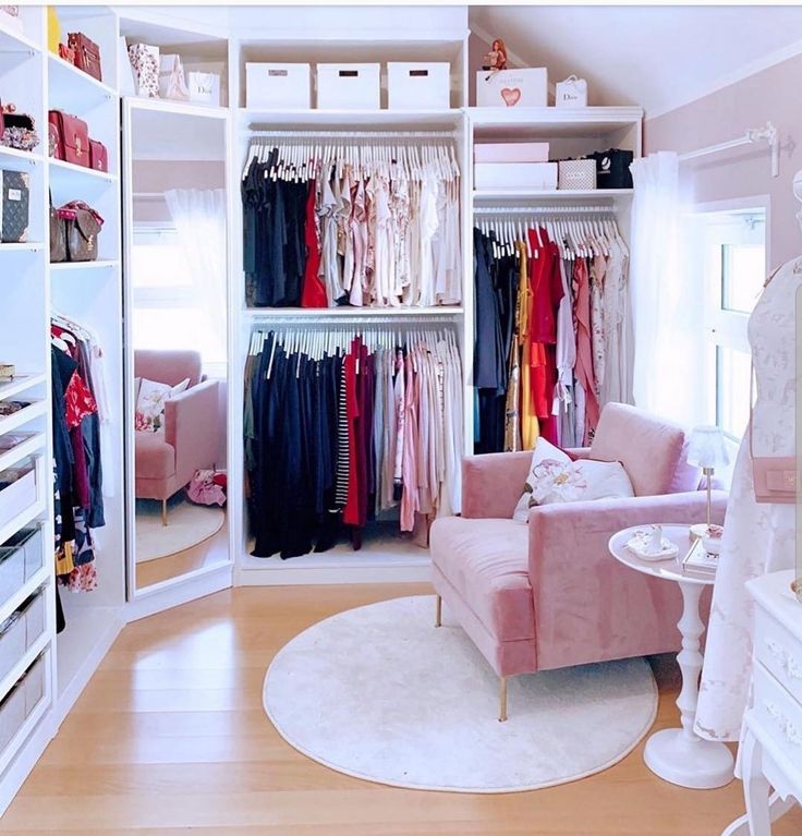 an organized closet with clothes on hangers, and a pink chair in the corner