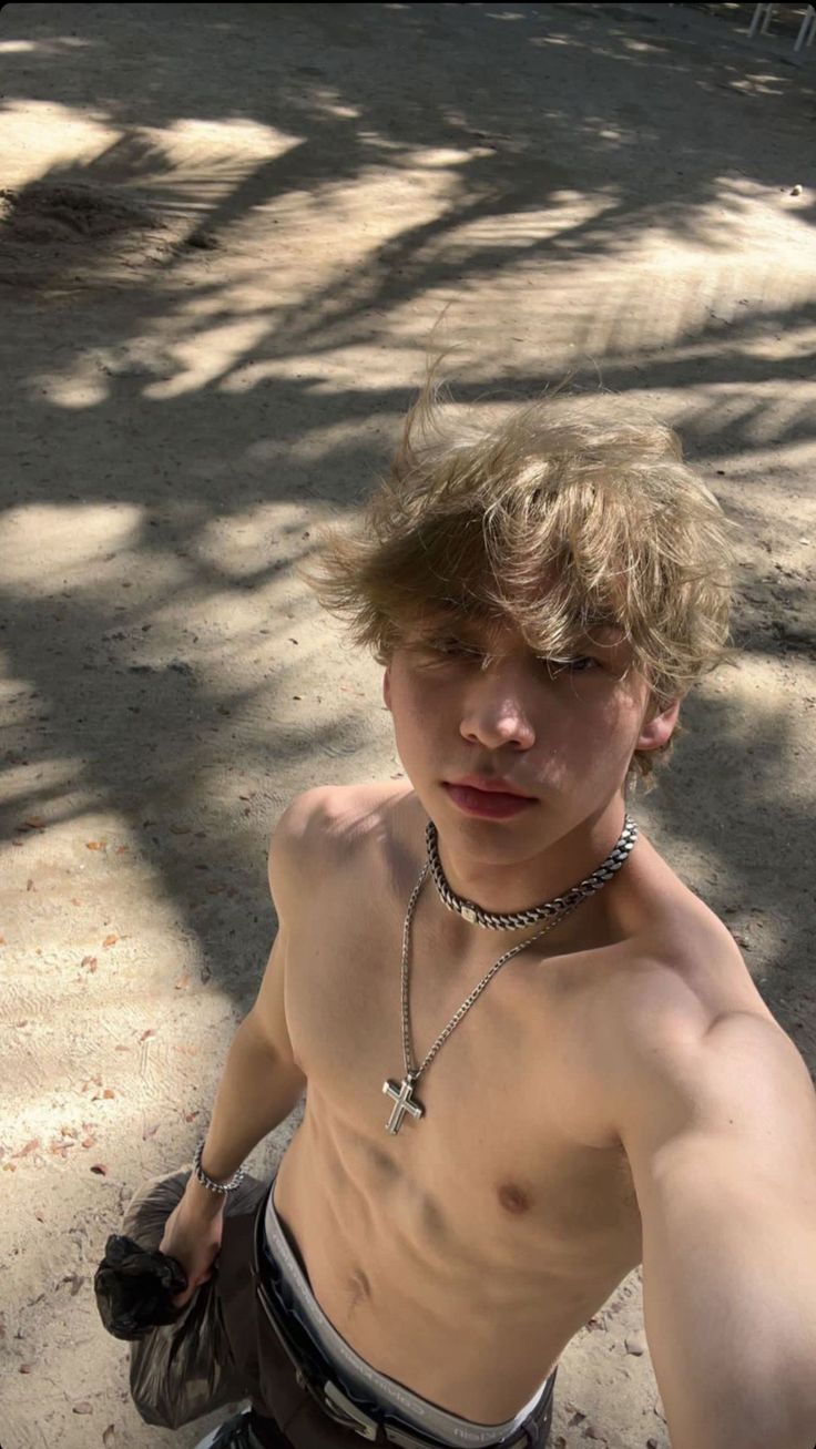 a shirtless young man sitting on top of a skateboard next to a tree