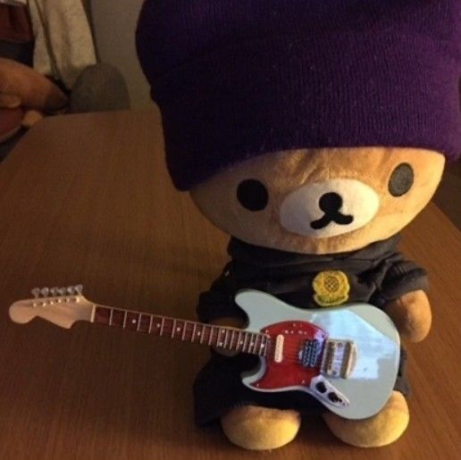 a teddy bear wearing a purple hat and holding a guitar in its lap, while sitting on a table