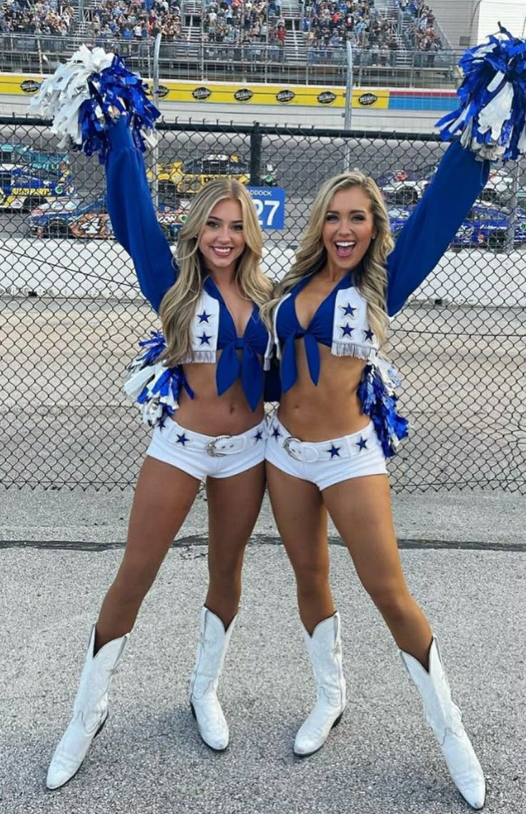 two cheerleaders in blue and white outfits posing for the camera at a football game