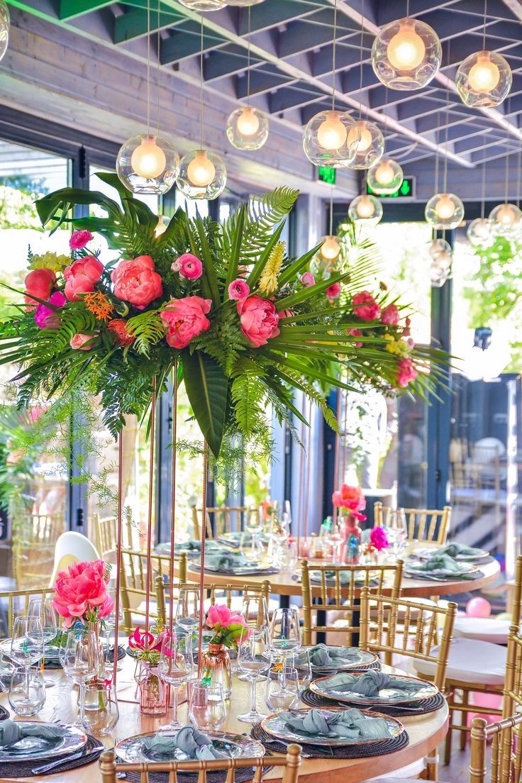 a table is set with plates and flowers in vases on the tables, surrounded by hanging lights