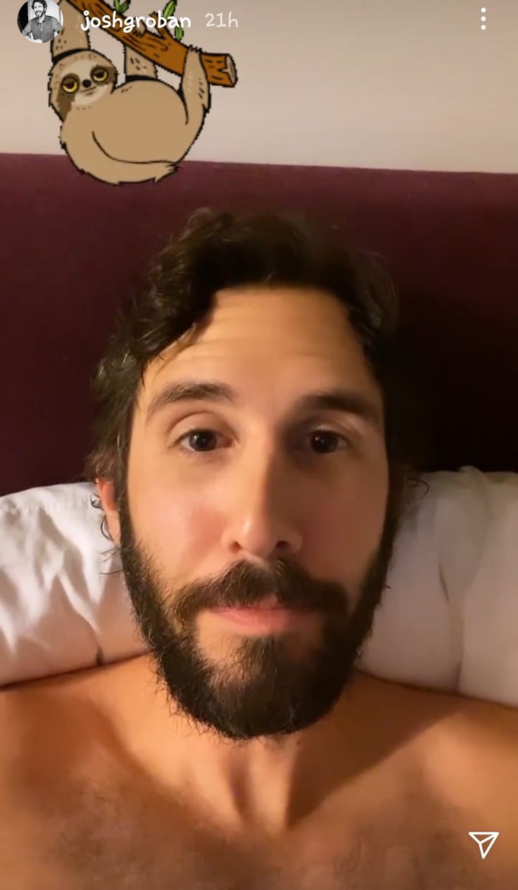 a man with a beard and no shirt on laying in bed looking at the camera