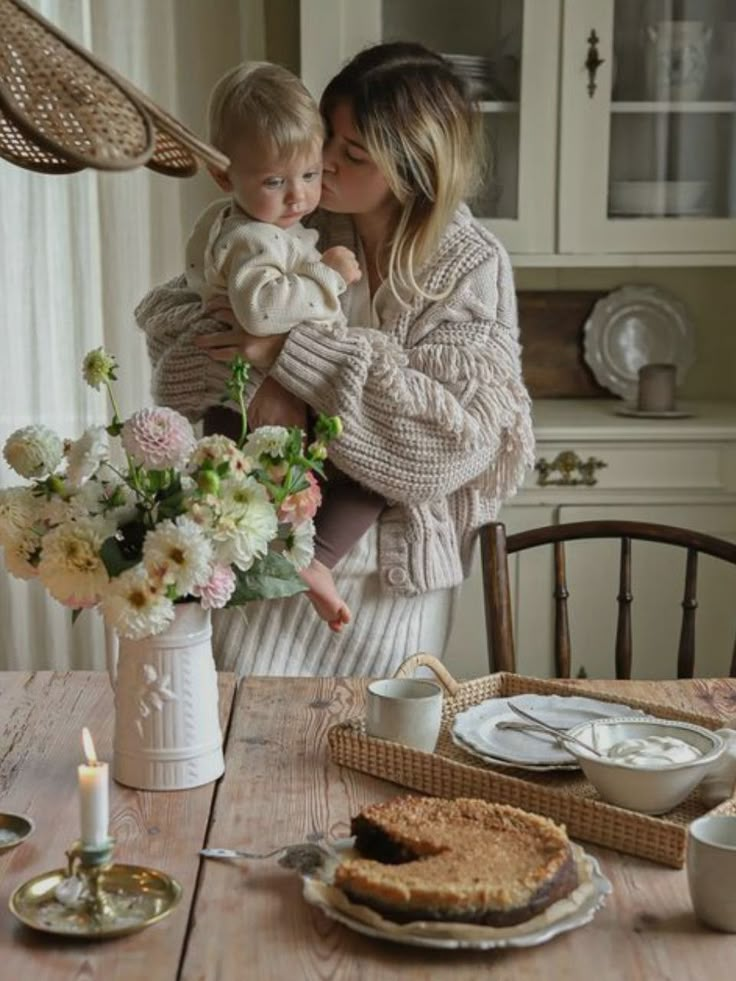 a woman holding a baby standing next to a table