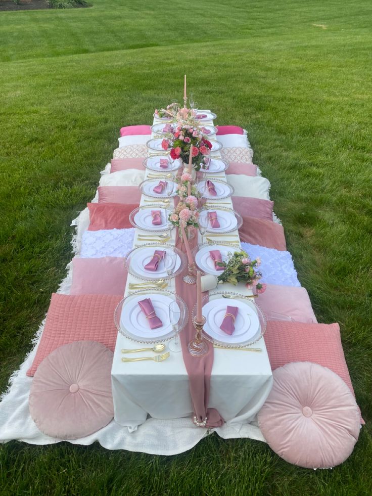 a long table set up with pink and white plates, napkins and place settings