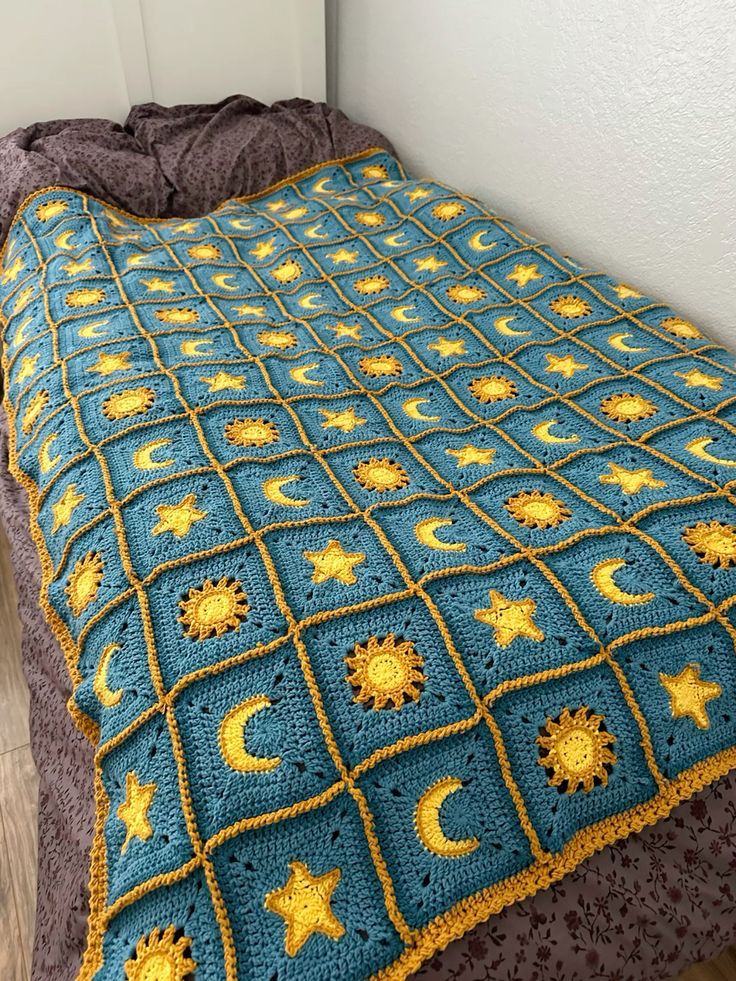 a blue crocheted blanket with yellow stars and crescents on it, next to a bed