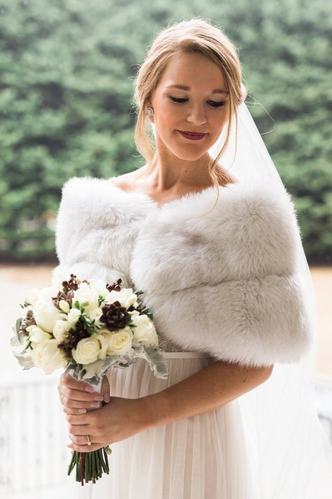 a woman in a wedding dress holding a bridal bouquet and fur stoler over her shoulder